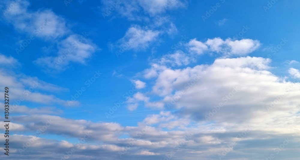 Fototapeta premium Blue sky with scattered white clouds. Natural background with soft cloud formations. Weather and atmosphere concept.