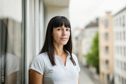 Free Download A woman with long dark hair stands thoughtfully on a balcony overlooking a city street during a calm morning, enjoying the tranquility - GFXLoad