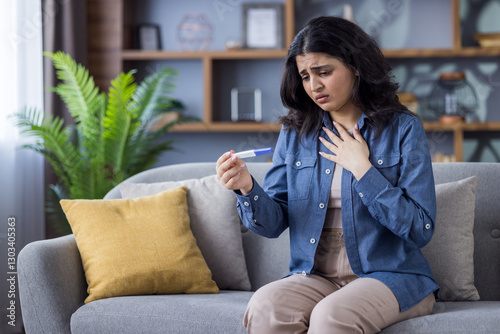 A young woman looks anxiously at a pregnancy test while sitting on the sofa in her living room. photo