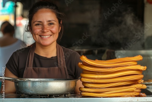 A smiling female churros seller behind her counter in an outdoor street market with a stack of churros
