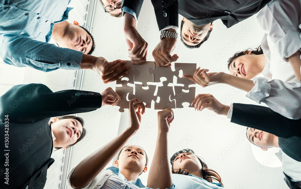 Fototapeta premium Multiethnic business people holding jigsaw pieces and merge them together as effective solution solving teamwork, shared vision and common goal combining diverse talent. Below view. Habiliment