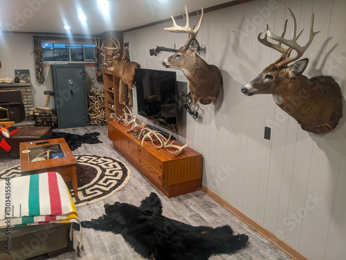 A cozy, rustic-themed room showcasing mounted deer heads, bear rugs, antler decor, and wood accents, providing a warm and natural hunting lodge ambiance.