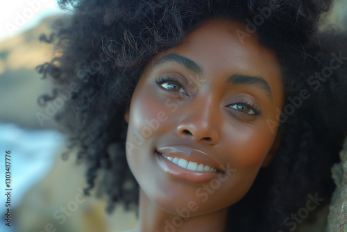Smiling young Black woman with curly hair, exuding warmth and joy against a natural outdoor backdrop.