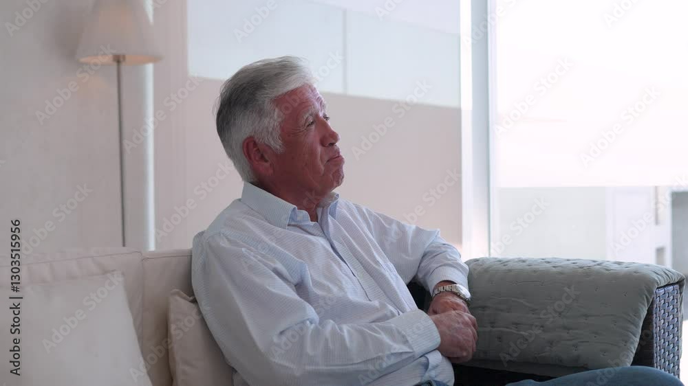 Pensive senior man sitting on comfortable sofa at home talking and listening, looking away Pensive senior man sitting on comfortable sofa at home talking and listening, looking away