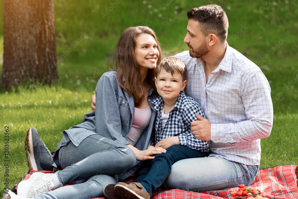 Fototapeta premium Loving family with adorable child spending weekend together on picnic at park