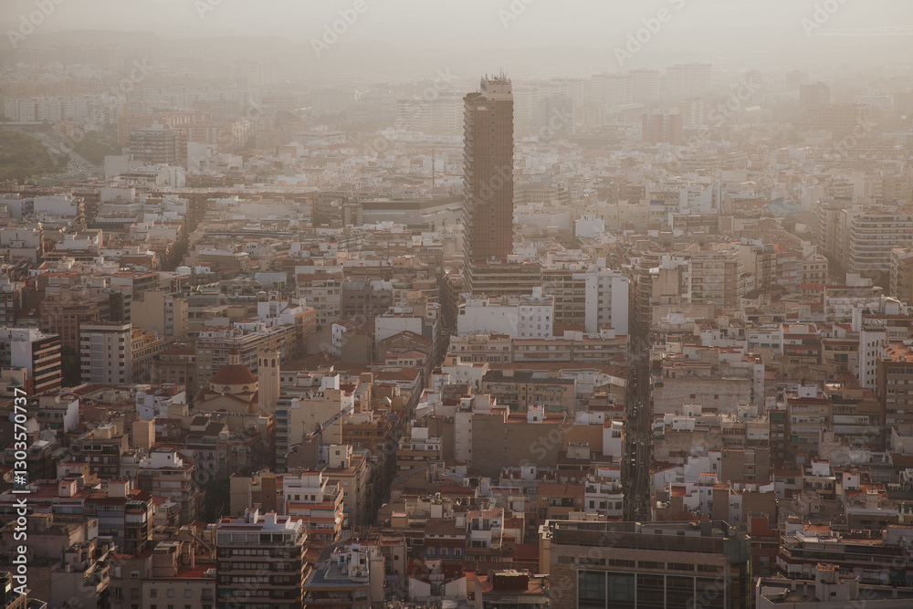 Fototapeta premium Aerial view of a dense urban landscape in Alicante, Spain, with a tall skyscraper standing among low-rise buildings under a hazy sky