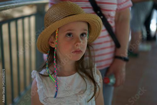 A sad little girl in a straw hat with small multicolored braids in a summer park. Concept of childhood emotion.