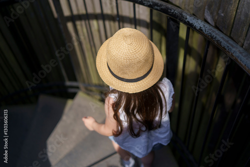 A little girl in a straw hat is descending a spiral staircase in a park. Top-down view. Concept of children's activity.