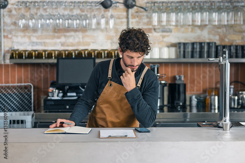 Handsome waiter taking inventory of everything missing while making a checklist on his phone at the coffee shop