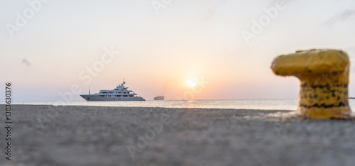Luxury boat moored off pier on Kos coastline with Blue Star Ferry in background and defocused yellow bollard in foreground