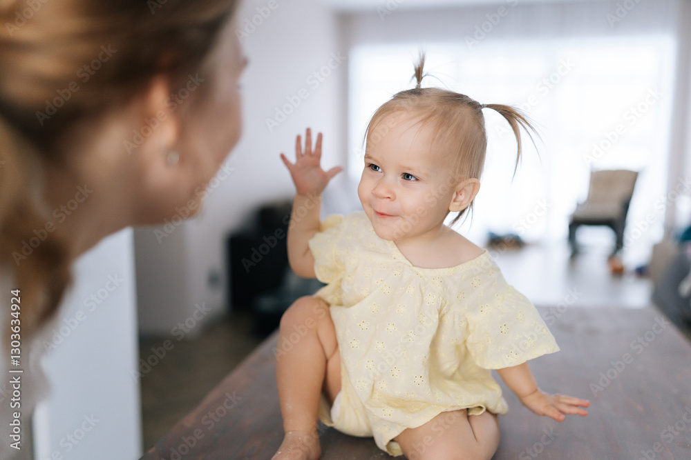 Fototapeta premium Portrait of pretty child girl sitting on kitchen table, playfully touching mother nose with flour-covered fingers, creating heartwarming scene of family bonding during baking. Concept parenting love