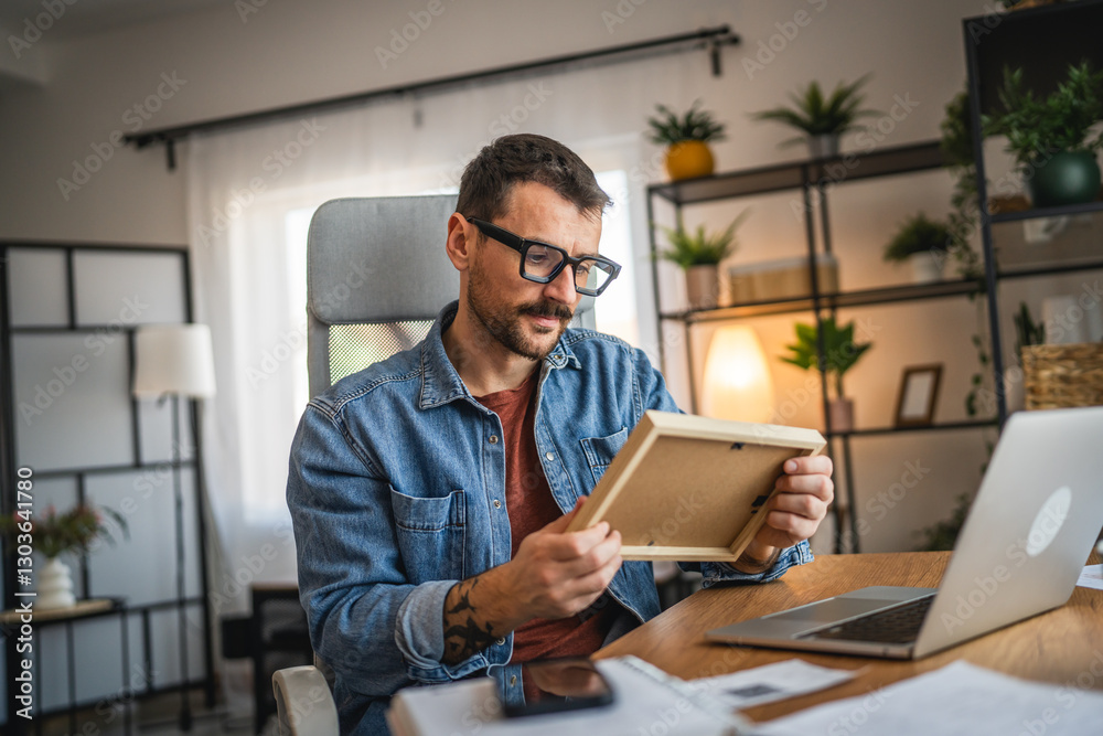 Fototapeta premium wistful man at home office nostalgic look at the photo frame