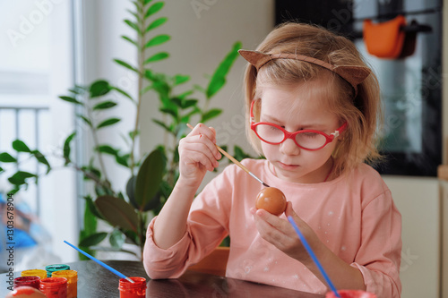 Girl painting Easter egg with bright colors using paint and brush, capturing creative and festive moment of holiday preparation. photo