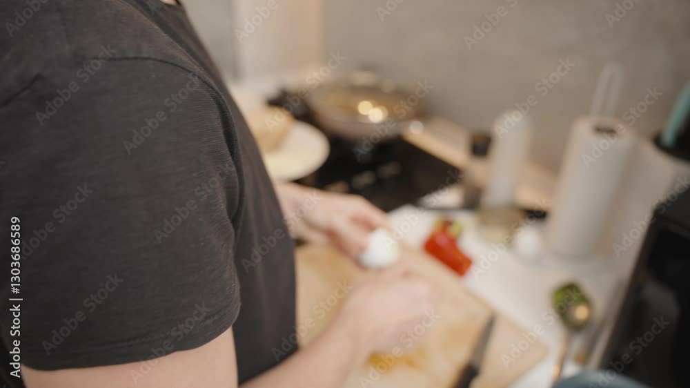 Woman in Black T-Shirt Peeling Hard-Boiled Egg Over Wooden Cutting Board in Modern Kitchen with Stove and Ingredients Nearby
