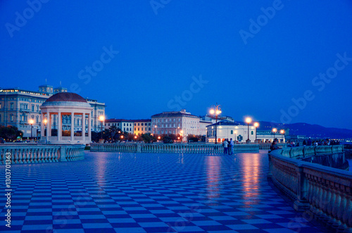 The iconic Terrazza Mascagni in Livorno at dusk. The vast checkerboard pavement and elegant gazebo are beautifully illuminated against a deep blue twilight sky.