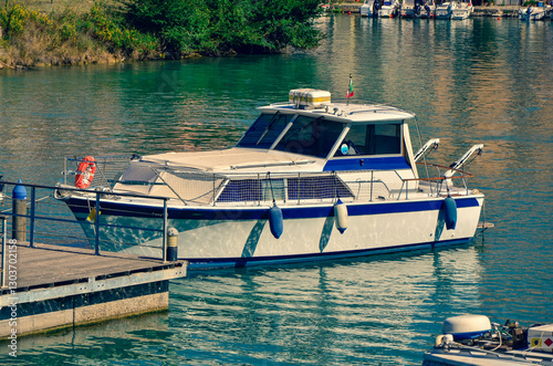 A white and blue motorboat is moored to a wooden pier in a calm harbor on a sunny day, evoking a peaceful atmosphere of leisure and recreation on the water.