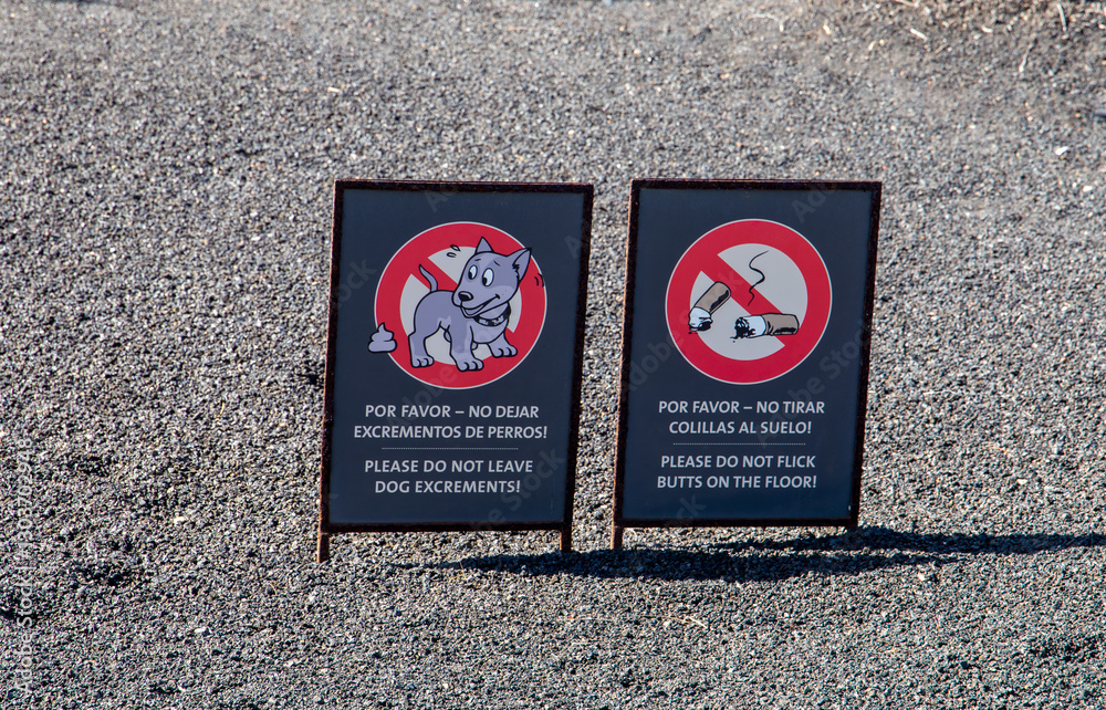 Bilingual signs urging not to leave dog excrement or flick cigarette butts on the ground on a gravel path. Bilingual signs urging not to leave dog excrement or flick cigarette butts on the ground on a gravel path.