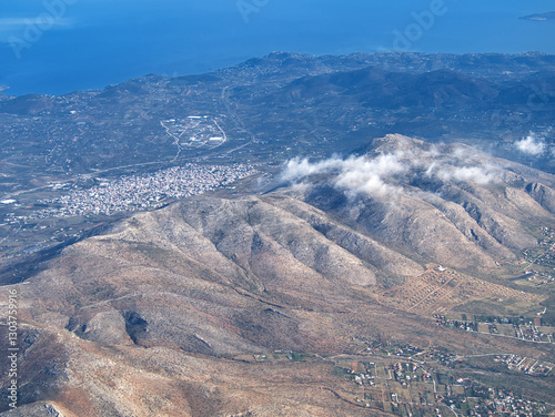 Aerial landscape of mountainous terrain with urban development near coastline and scattered clouds. Ymittos, Attica, Greece photo