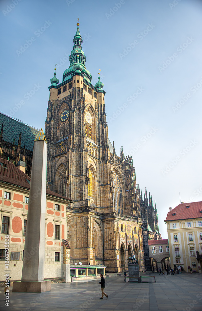 Fototapeta premium The magnificent, Gothic St. Vitus Cathedral stands tall under a bright blue sky, featuring intricate architectural details and green-tipped spires on a summer day in Prague, Czech Republic.