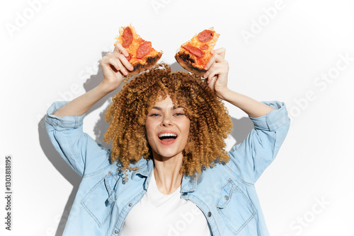 Joyful young woman with curly hair holding pizza slices, celebrating fun and delicious food moments in a bright, white setting