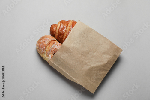 Fototapeta Naklejka Na Ścianę i Meble -  Paper bag with fresh baguette and croissant on gray table, top view