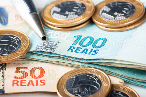 Close-up shot of Brazilian Real banknotes and coins with a pen, illustrating finance, economy, or business concepts in Brazil