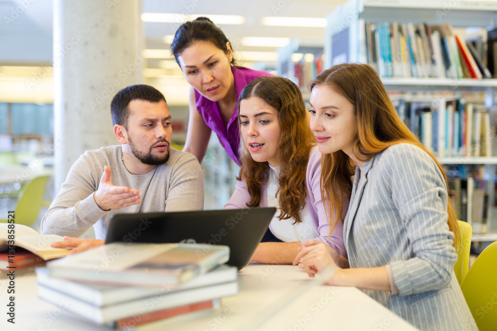 Friendly group of students studying in the university library is preparing for classes on a laptop, discussing current issues Friendly group of students studying in the university library is preparing for classes on a laptop, discussing current issues