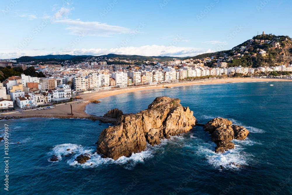 Obraz premium Picturesque aerial view of Blanes cityscape on Mediterranean coast overlooking symbol of city, Sa Palomera Rock and San Juan hill with tower of medieval castle on sunny day, Catalonia, Spain..