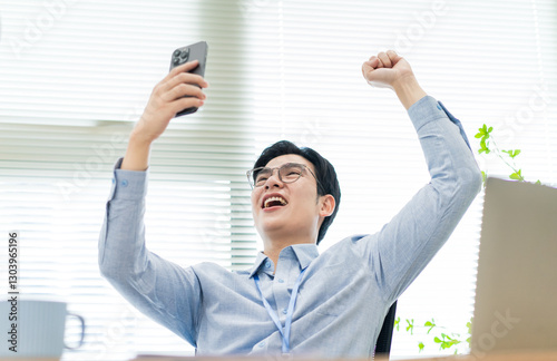 Excited young man celebrating success while using smartphone in a bright office environment
