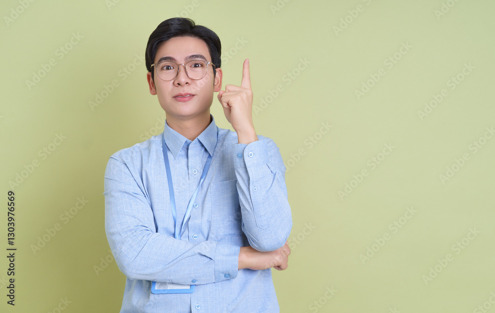 Young man gestures upward while standing against a green background, demonstrating a moment of inspiration or realization Young man gestures upward while standing against a green background, demonstrating a moment of inspiration or realization