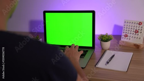 Laptop Workspace with Green Screen: A person engrossed in their work, typing on a laptop with a vibrant green screen on a sleek wooden desk. This setup is perfect for designers, entrepreneurs.