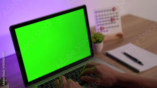 Working on a Green Screen Laptop: A person diligently types on a laptop, its screen displaying a vibrant green, suggesting seamless integration of digital content, creating a modern.