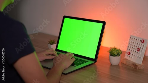 The Green Screen Workspace: A person at a desk typing on a laptop with a green screen, ready to showcase digital content and immerse viewers in a versatile display. 