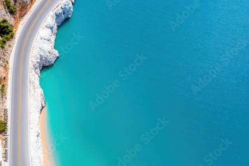 Aerial view of a winding coastal road next to a beautiful turquoise sea, with rocky formations and sandy beach areas visible.