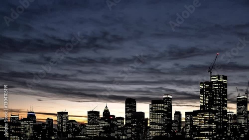 A time lapse of a city skyline captures skyscrapers as they shift from shadow to light, showcasing the sun rising and casting vibrant hues across the sky. For intro, transitions, or mood setting
