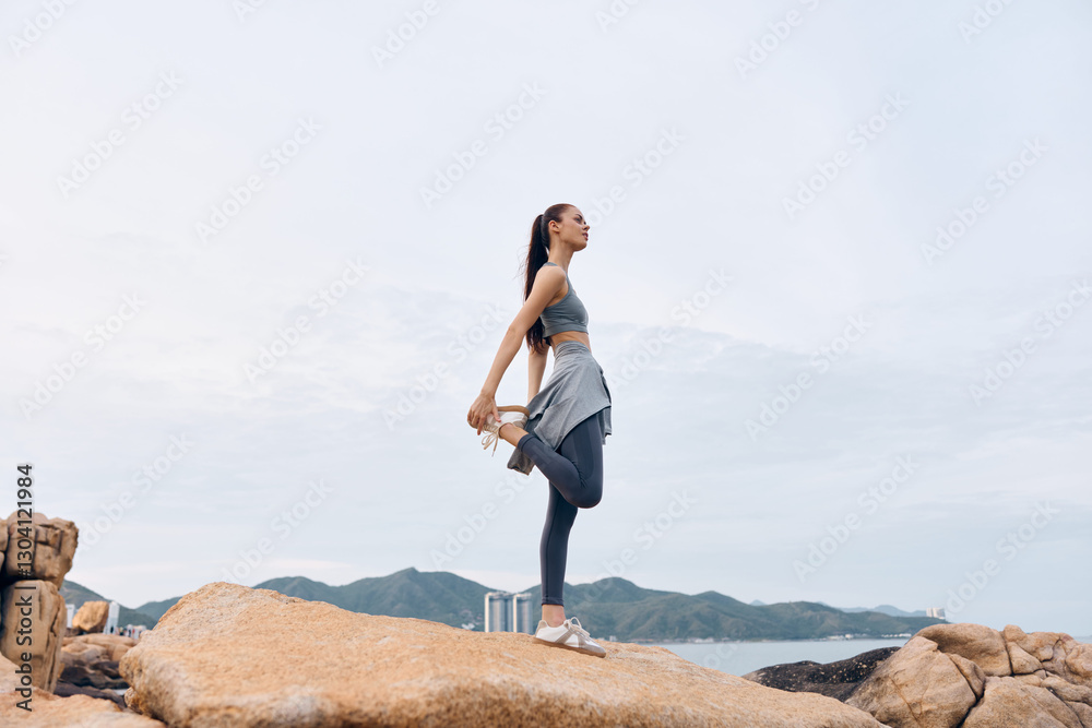 Young Asian woman practicing yoga outdoors on rocky terrain, wearing sportswear, showcasing flexibility and serenity with a serene backdrop of mountains Young Asian woman practicing yoga outdoors on rocky terrain, wearing sportswear, showcasing flexibility and serenity with a serene backdrop of mountains