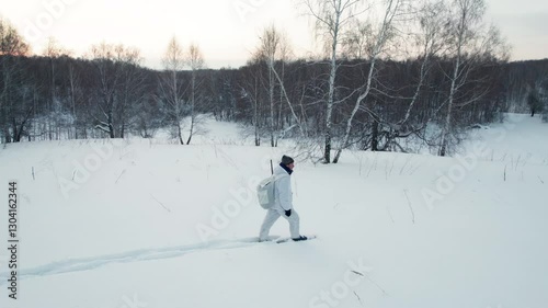 Hunter in snowshoes and winter camouflage walking across the field
