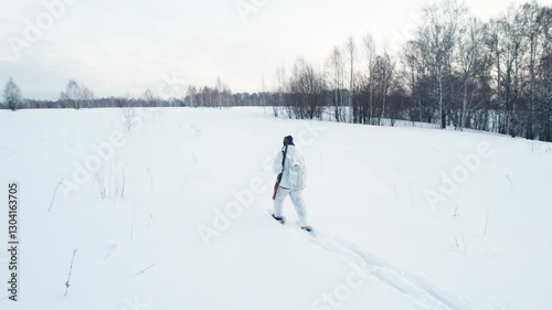 Hunter in snowshoes and winter camouflage walking across the field