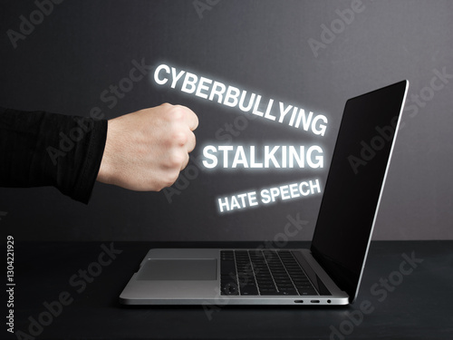 Fist hitting laptop screen with cyberbullying, stalking and hate speech texts