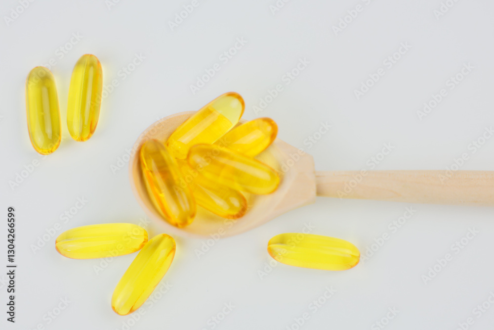 A close-up view from above of yellow omega-3 fish oil capsules lying in and around a wooden spoon on a white background. The concept of vitamins, dietary supplements, self-care. High quality photo A close-up view from above of yellow omega-3 fish oil capsules lying in and around a wooden spoon on a white background. The concept of vitamins, dietary supplements, self-care. High quality photo