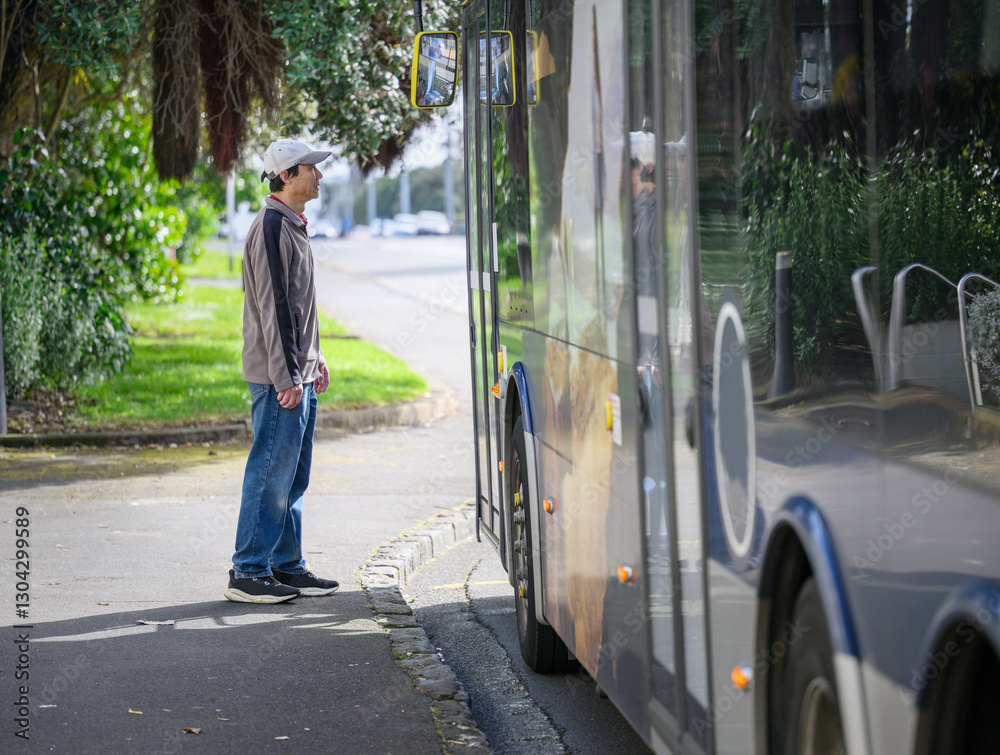 Man waiting to board the bus at bus stop on a leafy city road. Auckland.