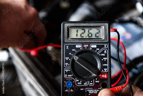 Mechanic holding voltmeter to check voltage car battery. Car repair.