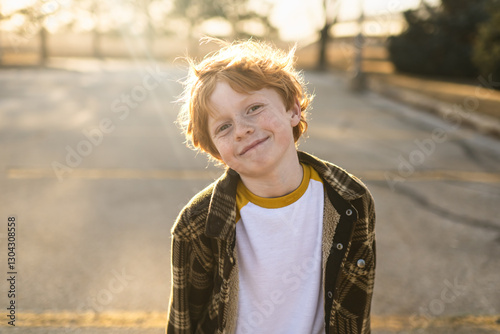 Little red head boy with sweet smile standing in sunny parking lot photo