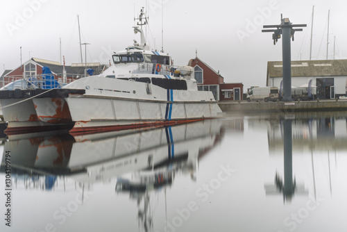 Harbor View with Docked Boat on Calm Reflective Water Surface, Foggy Background, Juelsminde, Denmark photo