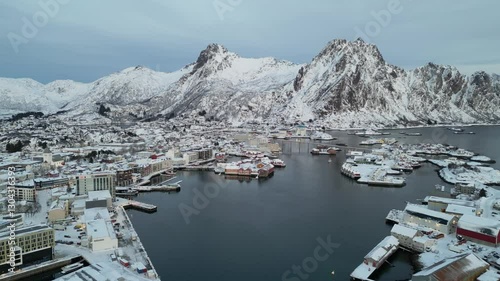 Svinøya village surrounded by snow-covered mountains and a calm harbor , aerial view photo