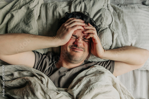 Man with headache lying in bed in the morning with hands on head