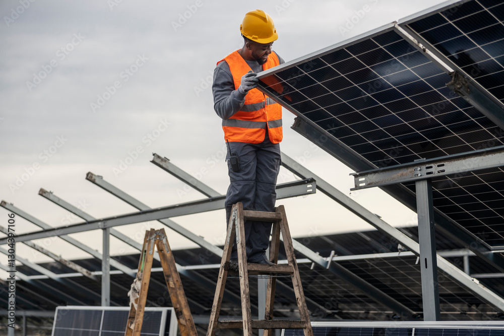 A young black worker on ladders installing solar panels at solar farm. A young black worker on ladders installing solar panels at solar farm.
