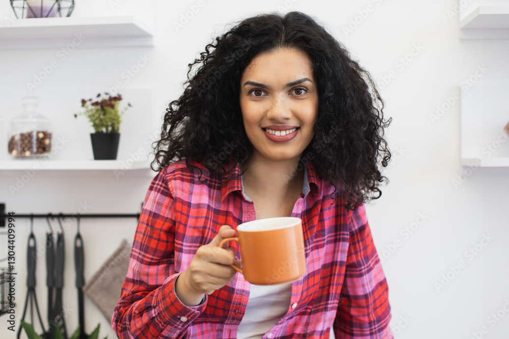 Young African American woman with curly hair wearing plaid shirt holding orange mug in kitchen. Smiling and happy expression capturing casual and warm moment. Young African American woman with curly hair wearing plaid shirt holding orange mug in kitchen. Smiling and happy expression capturing casual and warm moment.