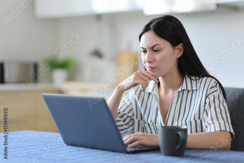Suspicious asian woman using laptop in the kitchen