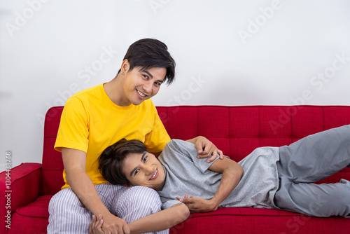 Asian LGBTQ gay couple enjoying a romantic and affectionate moment on a red sofa, looking at camera